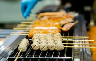 Closeup pork balls wood stick with small sausage grilling on electric stove for sell in food market. photo