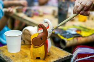 primer plano de las manos de los estudiantes de arte que sostienen el estudio de pinceles de pintura y aprenden a pintar sobre muñecas de animales de madera en el aula de arte. foto