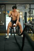 Closeup Asian handsome man workout training the battle rope in fitness center. photo