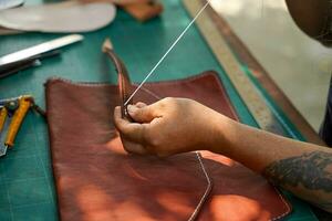 de cerca y cosecha manos de cuero artesano de coser un cuero marrón bolso para un cliente. foto
