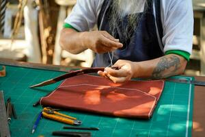 de cerca y cosecha manos de cuero artesano de coser un cuero marrón bolso para un cliente. foto