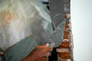 Closeup hands of builder holding mortar pan and plastering walls with cement in construction site. photo