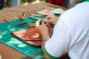 de cerca y cosecha manos de cuero artesano de coser un cuero marrón bolso para un cliente. foto