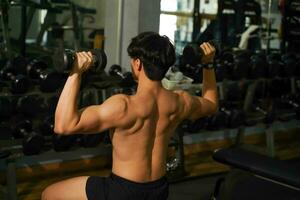 Closeup back view perfect body of Asian guy playing weight training at fitness center. photo