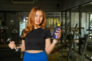 Young female relax and holding vitamin water bottle after fitness training at the fitness center photo