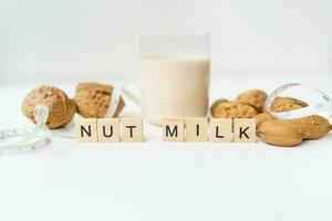 Vegan milk from nuts in a glass cup with various nuts on a white table. Lettering nut milk. photo