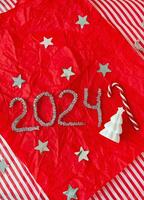 The inscription for the New Year 2024 on a red background along with a ceramic Christmas tree and a candy cane. Vertical photo. photo