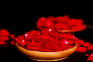 Rose petals in a bowl on a table with a black background photo