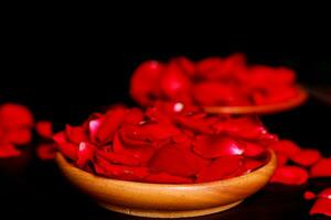 Rose petals in a bowl on a table with a black background photo