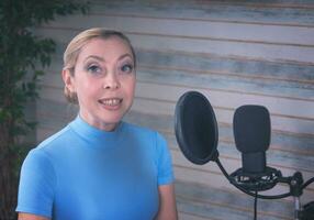 A girl in a blue turtleneck is preparing for a podcast with a microphone. Large ficus in the background photo