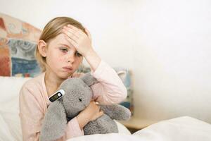 Sad little girl measuring temperature with digital thermometer photo