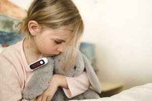 pequeño niña medición temperatura con digital termómetro. niño enfermo y tiene alto temperatura foto