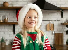 Happy child in Santa hat laughing and looking sideways in domestic kitchen interior photo