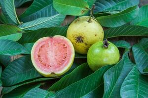 Fresh red guava with green leaves on wooden background. Texture of wood and guava leaves. photo