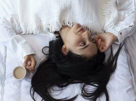 Beauty woman drinking coffee in bed after waking up in morning. Young beautiful woman in bed with cup of coffee. Cute lady waking up. Breakfast in a cozy bedroom photo