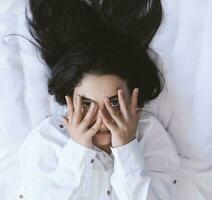 Beautiful woman lying in bed. Sexy black haired lady posing with her finger in mouth. Female enjoying, biting finger. Feeling happy, recreation, satisfaction and enjoyment. photo