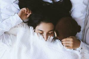 Young woman sleeping with toy bear. Cute black haired woman resting in bed with pleasure. Happy life of single lady. Pretty girl enjoying long sleep on her weekend photo