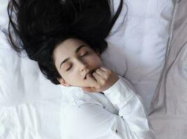 Beautiful woman lying in bed. Sexy black haired lady posing with her finger in mouth. Female enjoying, biting finger. Feeling happy, recreation, satisfaction and enjoyment. photo