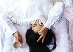 belleza mujer Bebiendo ordenando café en cama. hembra despertar arriba en Mañana. joven hermosa mujer en cama con taza de café. linda dama despertar arriba. desayuno en acogedor dormitorio foto