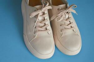 Universal women's beige light leather sneakers with laces on a blue background. Fashionable street shoes. photo