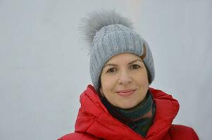 un joven caucásico mujer vistiendo un de punto gris invierno sombrero y rojo chaqueta sonrisas y mira a el cámara. foto