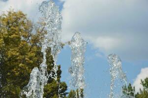 Fountain water jets on a summer day against the backdrop of green trees and blue sky. photo