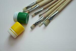 Gouache paints in closed jars and brushes on a white background. Items for drawing, creativity, hobby. photo