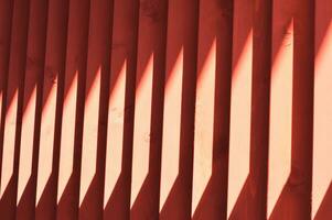 Red wooden slats. Abstract pattern with vertical lines and sunlight. Part of a bench, an element of building decor. photo