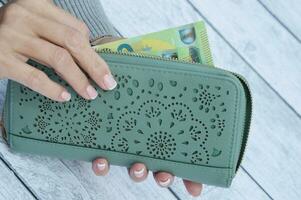 un mujer pone en o toma fuera dinero desde un verde cartera. billetes en un billetera foto