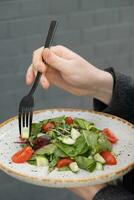 Woman eating fresh salad with arugula, cherry tomatoes, cucumbers in a plate, closeup photo