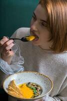 A young woman eats pumpkin puree soup in a restaurant. Autumn menu concept photo