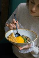 A young woman eats pumpkin puree soup in a restaurant. Autumn menu concept photo