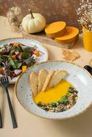A plate of mashed pumpkin soup and salad. Autumn menu concept photo