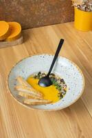 A plate of mashed pumpkin soup on wooden table. Autumn menu concept photo