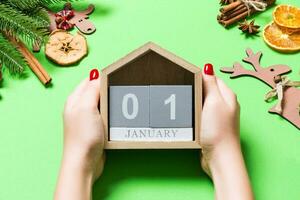 Top view of female hands holding calendar on green background. The first of January. Holiday decorations. New Year concept photo