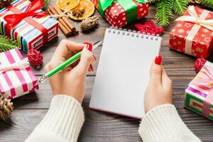 Top view of female hand writing in a notebook on wooden Christmas background. Fir tree and festive decorations. Wish list. New Year concept photo