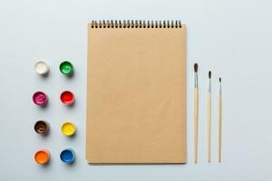 Album pages and paints, pencils, brush on a colored background. Top view with empty space. workplace for creativity. home teaching concept drawing photo