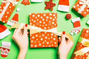 Top view of female hands holding a Christmas present on festive green background. Santa hats and holiday decorations. New Year holiday concept photo