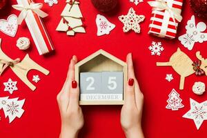 Top view of female hands holding calendar on red background. The twenty fifth of December. Holiday decorations. Christmas time concept photo