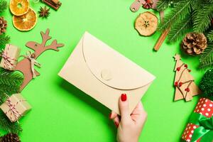 Top view of woman holding an envelope on green background made of holiday decorations. Christmas time concept photo