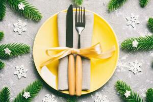 Top view of New Year dinner on festive cement background. Composition of plate, fork, knife, fir tree and decorations. Merry Christmas concept photo