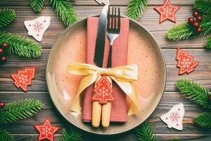 Top view of cutlery and plate on festive wooden background. New Year family dinner concept. Fir tree and Christmas decorations photo