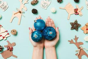 vista superior de un montón de bolas de año nuevo en manos femeninas sobre un fondo azul hecho de decoraciones festivas. concepto de tiempo de navidad foto