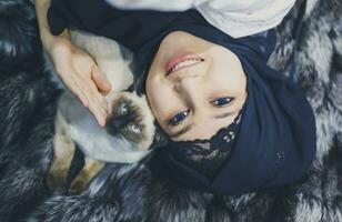 Attractive muslim girl plays with her exotic domestic Siamese cat photo