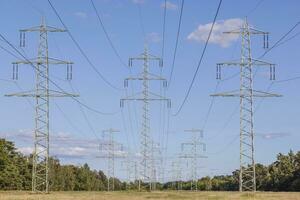 Image of an electricity pylon from the ground perspective in front of a blue sky with white clouds photo