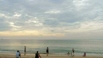 PHUKET, THAILAND FEBRUARY 26, 2023 Airplane over a crowded beach. Tourists take photos in front of a flying airplane. People, aircraft background. The concept of travel video