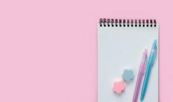 Blank notepad, colored pen and erasers on a pink background. Flatlay. Top view. Copy space. photo