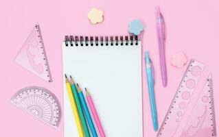 Flatlay composition with blank notepad and school stationery on a pink background. Back to school. Top view. Copy space. photo