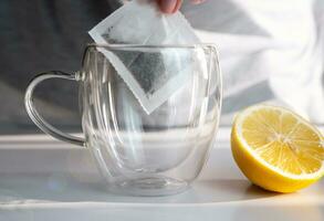 un muchachas mano pone un té bolso en un taza. negro té con limón en el Mañana. de cerca. selectivo enfocar. foto