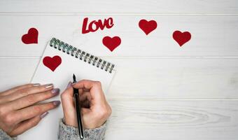 Woman's hands write a love letter on notepad. Romantic greeting for Valentine's Day. Valentine's Day holiday concept. Top view. Flatlay. Copy space. photo